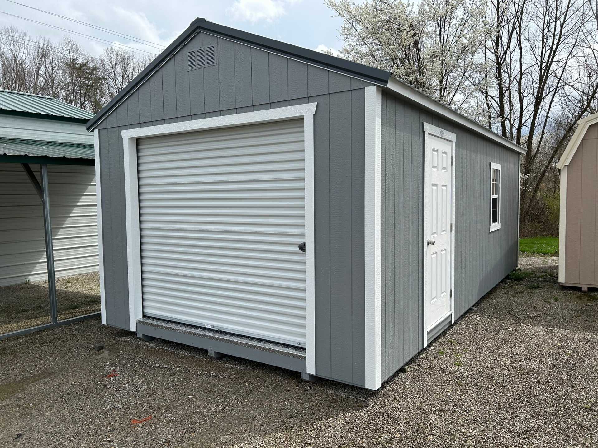 12x24 Classic Wood Garage. Gray Walls White Trim Slate Gray Roof. Options Include 8x7 Roll-up Door, Solid Panel Walk in Door, 1 - Window and Foil on Roof.